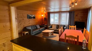 Ein gemütliches Blockhaus-Interieur mit einem Holzesstisch, einer Couch und einem Fernseher.