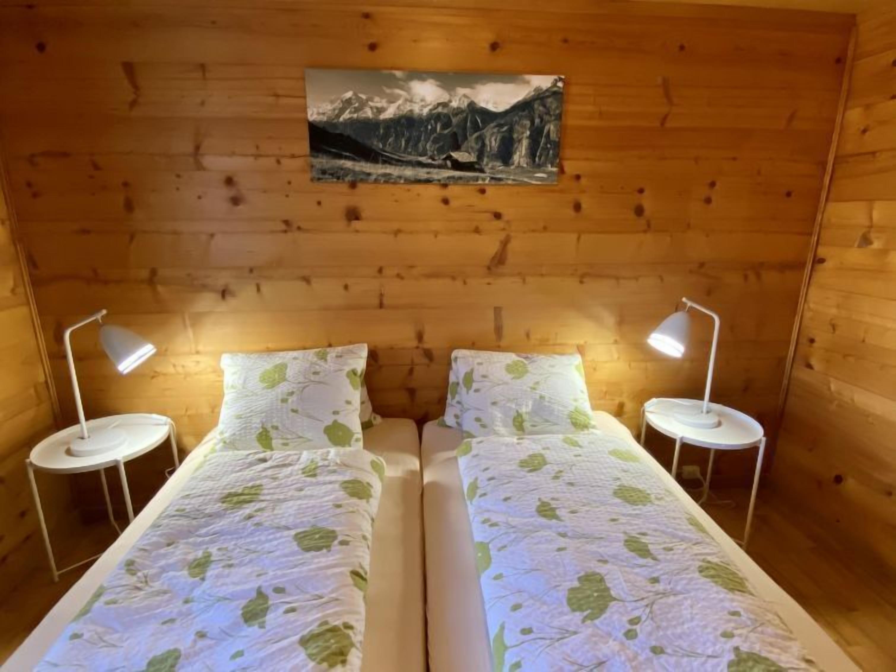 Une chambre de style cabane en bois, équipée de deux lits, chacun avec un oreiller et une lampe.