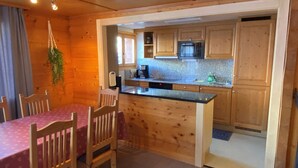 Eine kleine Küche mit Holzausstattung, einer Mikrowelle und einer Kaffeemaschine. Ein Esstisch mit Stühlen und eine hängende Pflanze sind ebenfalls vorhanden.