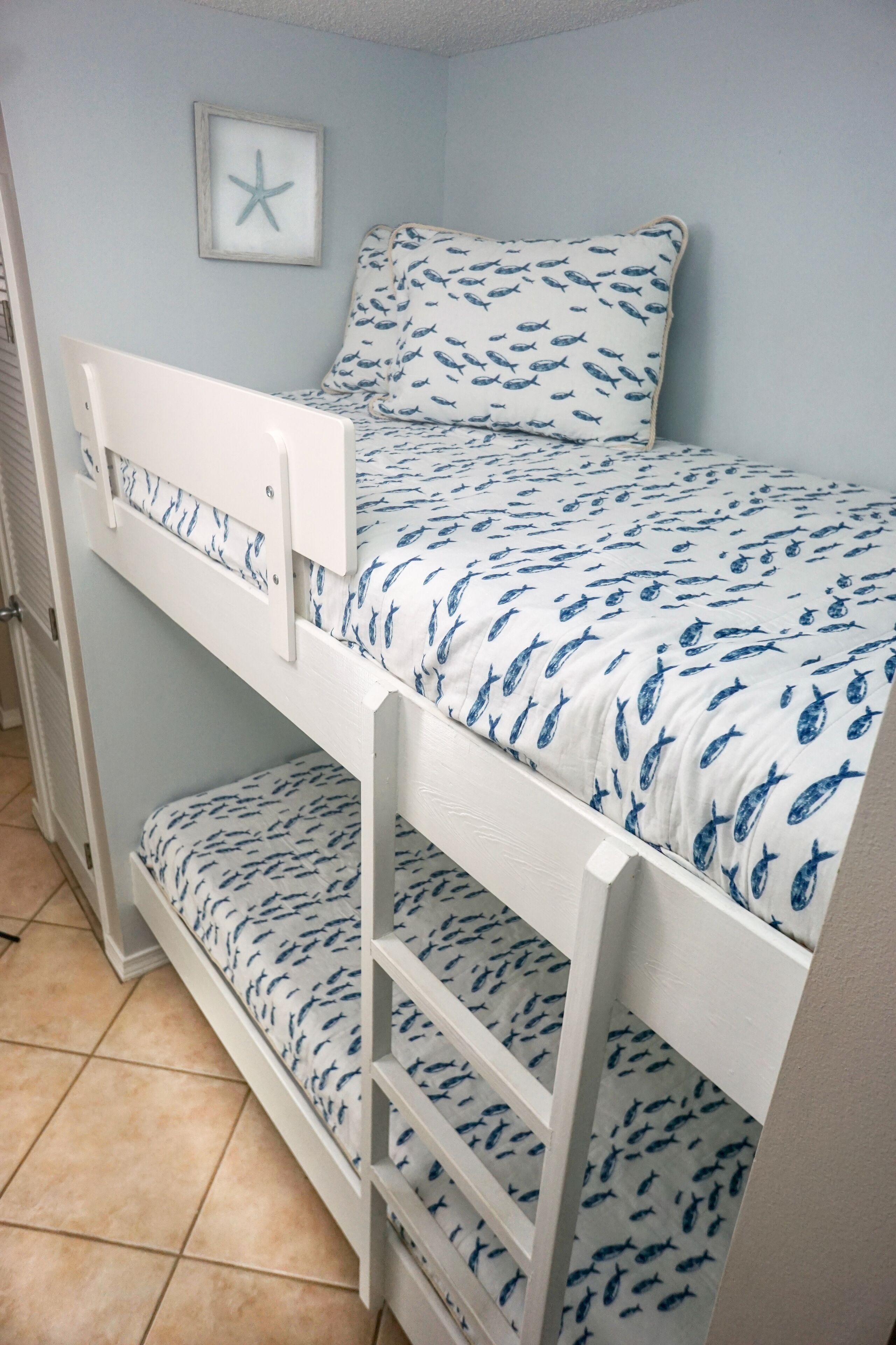 A bunk bed with a starfish decoration on the wall, a tiled floor, and a window with blinds.