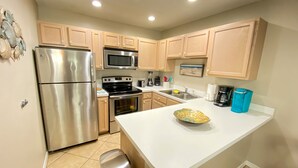 A modern kitchen with stainless steel appliances, wooden cabinets, and a white countertop. - The Turtles Escape (Destin)