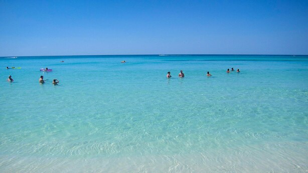 A beach with clear turquoise water and a few people swimming and relaxing. - The Turtles Escape (Destin)