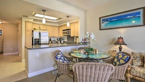 Una cocina con una isla central, zona de comedor con sillas de mimbre y una mesa de comedor.