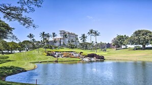Campo de golf con un estanque, palmeras y un edificio grande al fondo.
