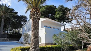 A modern two-story building with a white exterior, surrounded by well-maintained landscaping including a palm tree and various shrubs. - El Gato I by Interhome (Llançà)