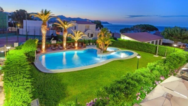 A swimming pool surrounded by well-maintained lawns and palm trees, with a view of the sea and mountains in the background. - El Gato I by Interhome (Llançà)