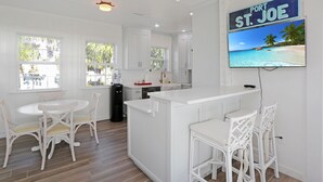 A kitchen with white cabinetry, a central island, and a dining area with white chairs. - Beachview in St Joe Beach, ~ Caroline's Cottage (St. Joe Beach)