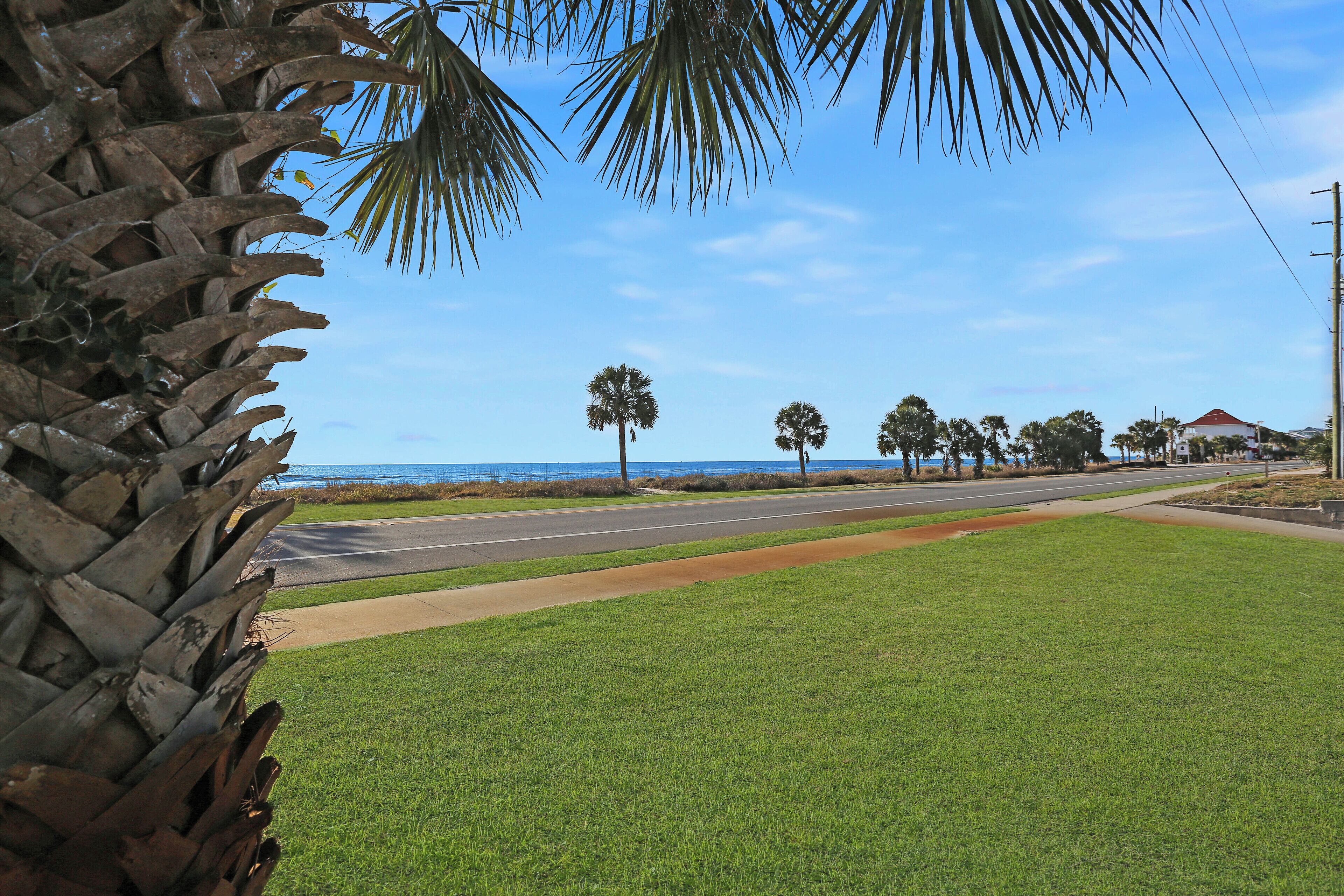 A coastal road with a grassy median, palm trees, and a clear blue sky.