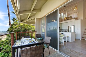 Ein Balkon mit Esstisch, eine Küchenzeile mit weißen Schränken und Blick auf das Meer.