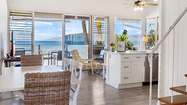 Amplia habitación con un gran ventanal corredero que da a un balcón con vistas al mar. Cuenta con un comedor con mesa y sillas, una cocina con armarios blancos y una escalera.