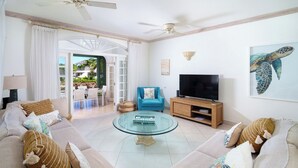 Un salón espacioso con una mesa de centro de vidrio, un sillón azul y un televisor sobre un soporte de madera.