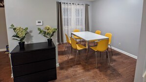 A dining area with a white table and yellow chairs, a black dresser, and two potted plants.
