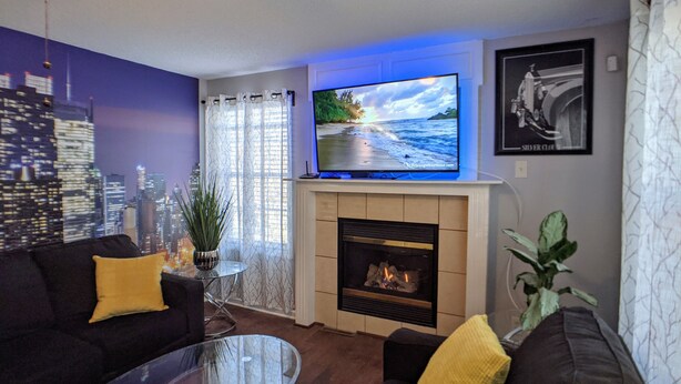 A living room with a fireplace, a television, and a cityscape mural on the wall.