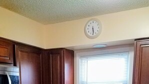 A kitchen with dark wooden cabinets, a stainless steel refrigerator, a microwave, a sink with a faucet, and a clock on the wall.