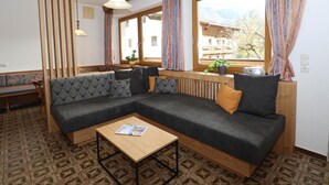 Un salon moderne avec un canapé d’angle, une table basse en bois et de grandes fenêtres avec des rideaux.