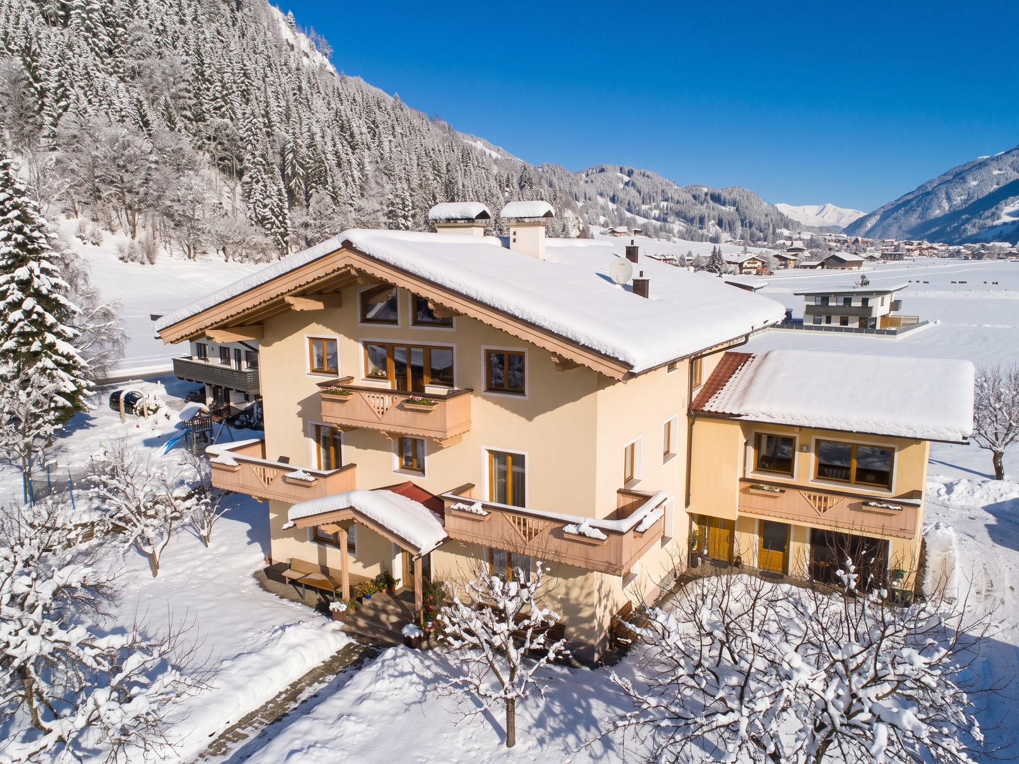 A multi-story chalet with balconies, surrounded by snow-covered trees and mountains.