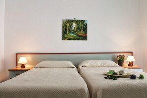 Two single beds with matching headboards and nightstands, each with a lamp and a small potted plant, complemented by a large framed picture on the wall.