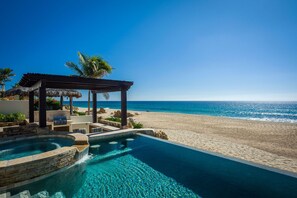 Une piscine avec vue sur la plage, une pergola et une structure dotée d’un toit de chaume.