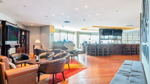A spacious living area with leather sofas, a coffee table, and a bar area with stools and a large TV screen. - Sea & City Views Takapuna Studio (Auckland)