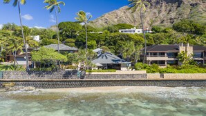 A coastal property with a stone wall, clear waters, and a mountain in the background. - Hale Makai at Diamond Head: Stunning Oceanfront Estate w/Private Pool & AC (Honolulu)