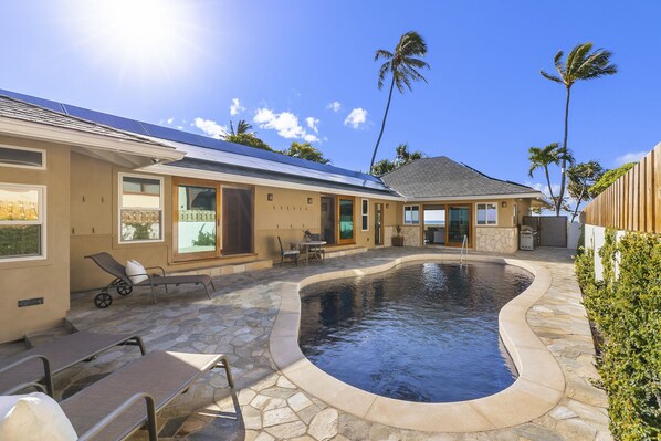 A residential property with a swimming pool, stone patio, and a house with large windows and a garage.
