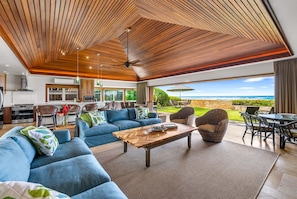 Relax in this spacious living area with a high ceiling, featuring a sofa set, coffee table, and wicker chairs, and enjoy the ocean view.