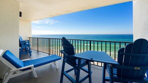 A balcony with blue chairs and a table, overlooking a clear blue ocean. - Commodore 802 (Panama City Beach)