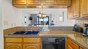 A kitchen with granite countertops, wooden cabinets, a dishwasher, and a coffee maker. - Commodore 802 (Panama City Beach)
