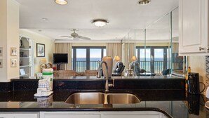 A modern kitchen with a large island, a dining area with a view, and a living room with a television. - Commodore 410 (Panama City Beach)