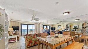 A spacious living room with a large table, comfortable seating, and a balcony with a view. - Commodore 410 (Panama City Beach)