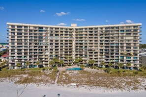 A multi-story hotel with balconies, a swimming pool, and a beach view.