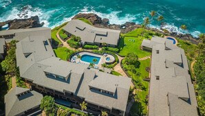 An aerial view of a resort with multiple buildings, a central swimming pool, and a view of the ocean. - Makahuena 5103 Oceanfront By Suite Paradise (Koloa)
