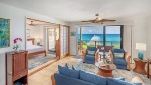 A hotel room with a bed, a sofa, a coffee table, and a view of the ocean. - Makahuena 5103 Oceanfront By Suite Paradise (Koloa)
