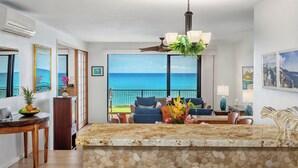 A kitchen with a stone countertop, a dining table, and chairs. There is a view of the ocean through large windows. - Makahuena 5103 Oceanfront By Suite Paradise (Koloa)