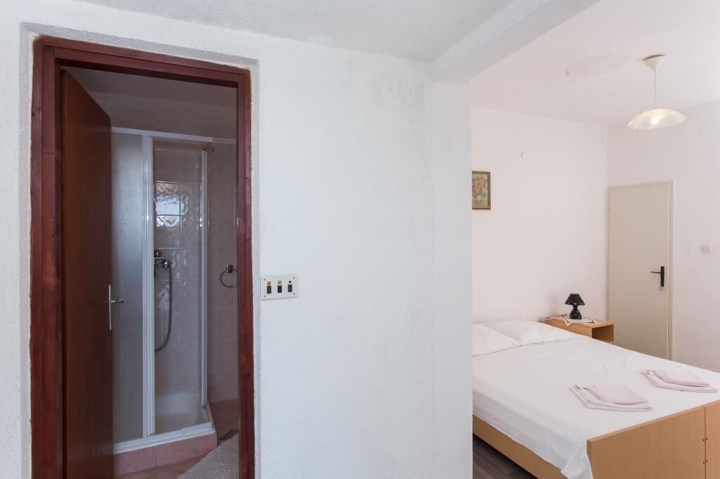 A bedroom with a bed, bedside table, lamp, and a shower area.