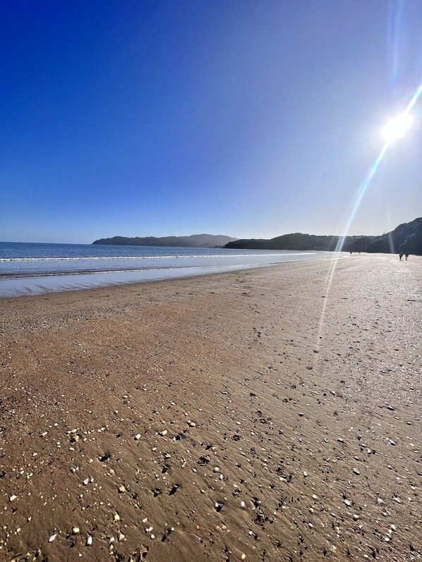 A beach with a clear sky and distant mountains. - Kupe Kottage (Coopers Beach)