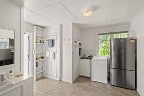 A compact kitchen with white cabinetry, a stainless steel refrigerator, a window with a view, and a built-in washing machine.
