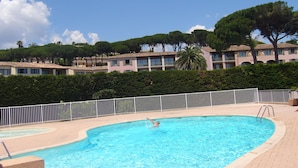 A swimming pool with a person swimming, surrounded by a white fence, with buildings and trees in the background.