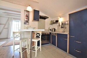 Une cuisine avec un plan de travail blanc, deux chaises blanches, une cuisinière, un four, un lave-vaisselle et des placards.
