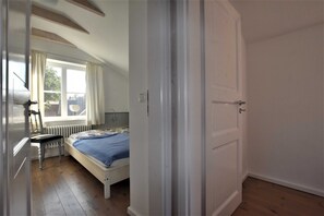 Une chambre avec un lit simple, un radiateur, une fenêtre avec des rideaux et une porte.