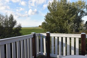 Une terrasse avec des rampes blanches et une vue sur un champ verdoyant et des arbres.