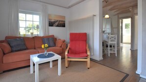 A living room with a sofa, a red chair, a small table with a vase, and a painting on the wall. - Ferienwohnung mit Meerblick, Balkon und Kamin OFC 06 - Nr. 3 Ferienwohnung mit Meerblick, Balkon und (Rerik)