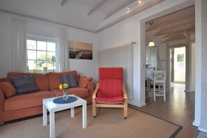 Un salon avec un canapé, un fauteuil rouge, une petite table sur laquelle se trouve un vase, et un tableau accroché au mur.