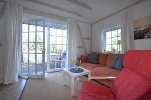 A living room with a red sofa, a white coffee table, and a large sliding glass door leading to an outdoor area.