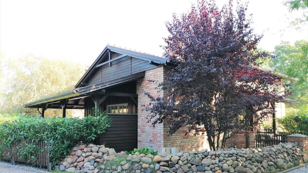 A rustic building with a stone facade, a wooden porch, and a stone wall in front. - Ferienwohnung mit Meerblick, Balkon und Kamin OFC 06 - Nr. 3 Ferienwohnung mit Meerblick, Balkon und (Rerik)