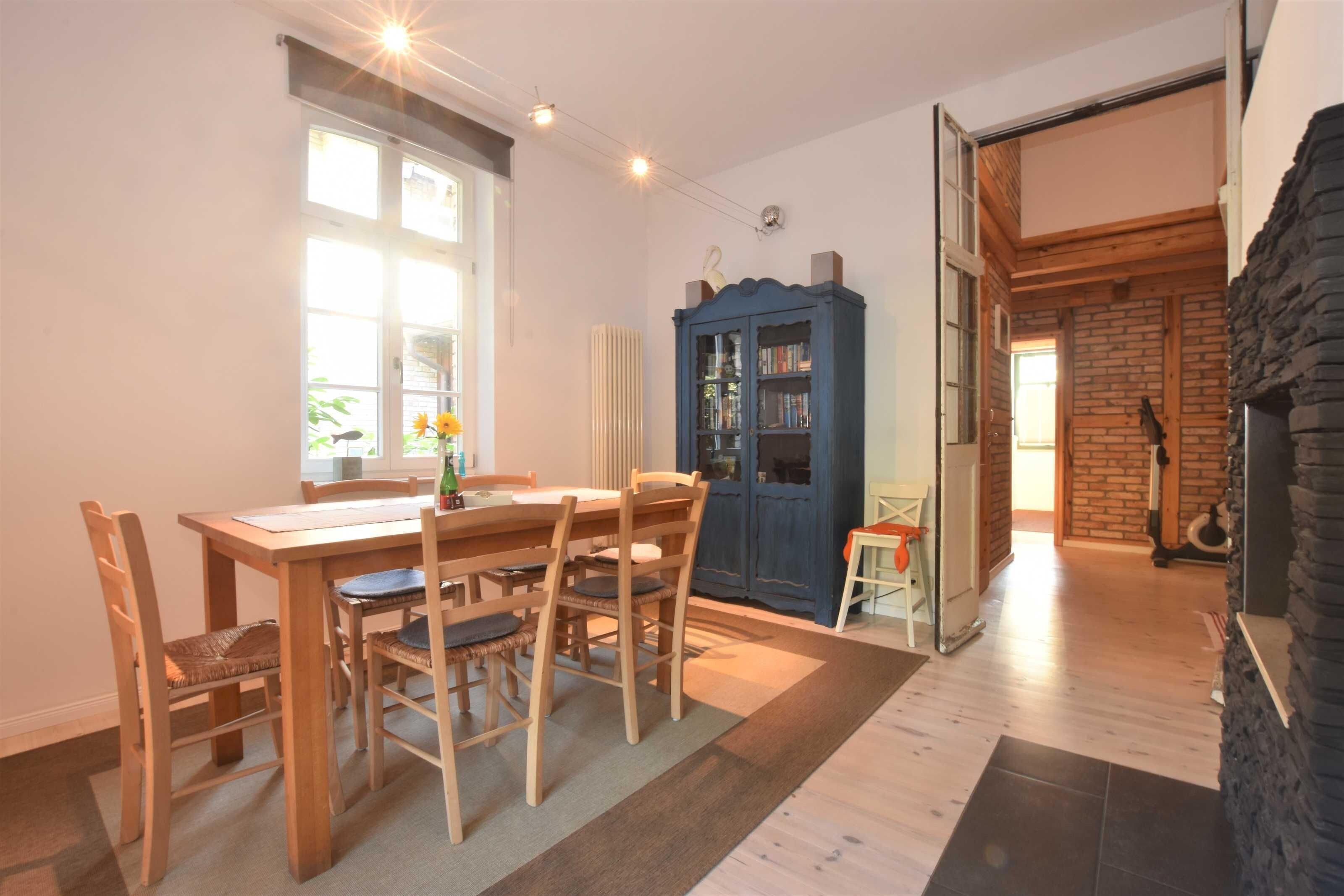 A dining area with a wooden table and chairs, a radiator, and a blue cabinet with glass doors.