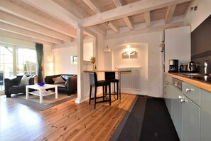 Eine moderne Küche mit Holzbalken, einem Essbereich mit weißem Tisch und einem schwarzen Sofa.