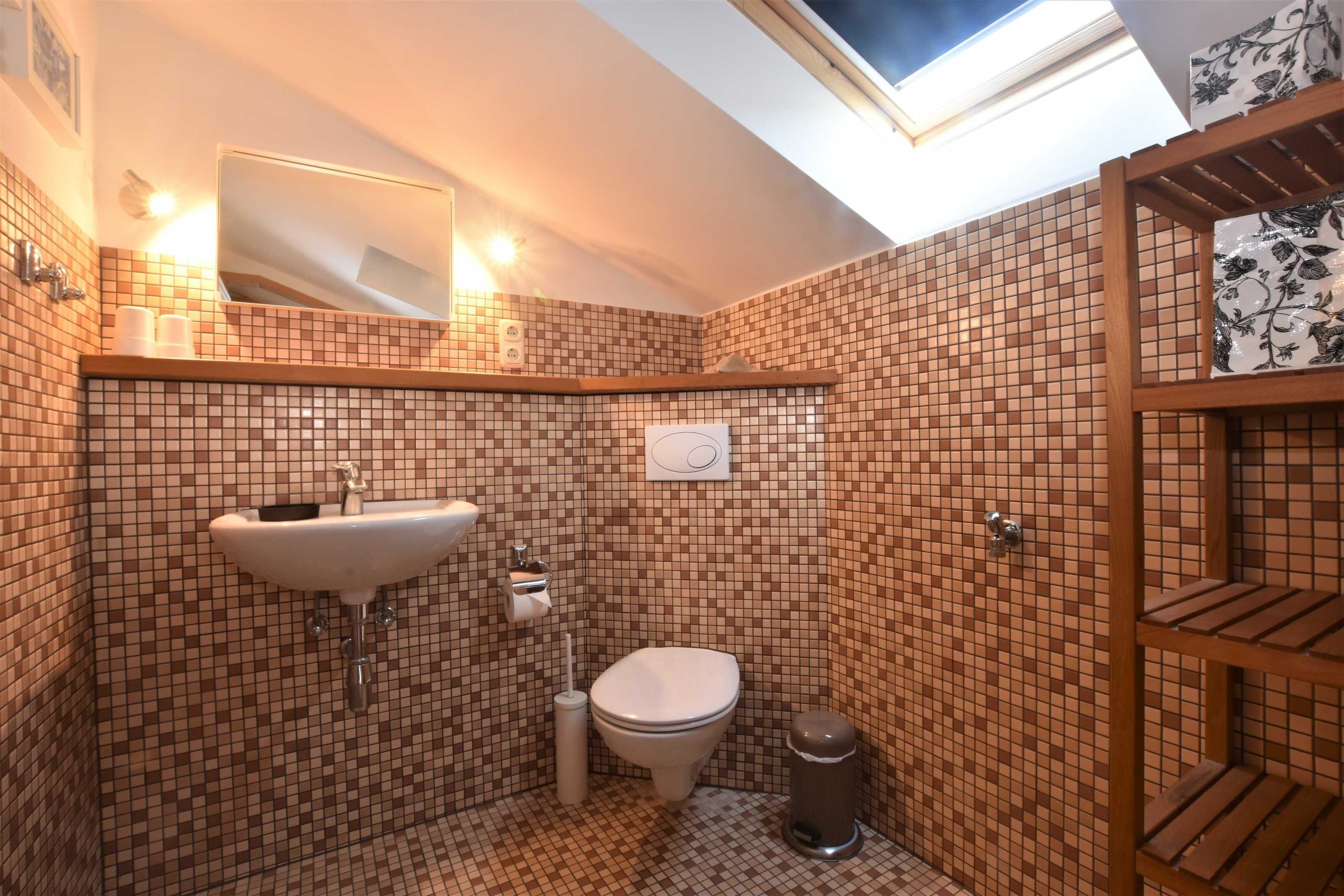 Une petite salle de bain avec un puits de lumière, un lavabo, des toilettes et une poubelle.