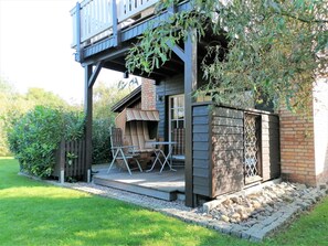 A wooden deck with a covered seating area and a stone pathway leading to a brick building.