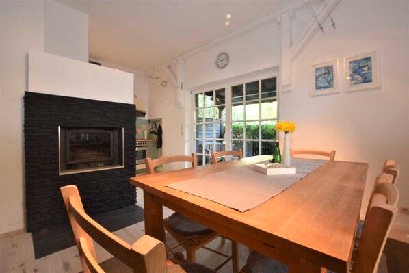 A dining area with a wooden table, chairs, a stone fireplace, and a window with a view of greenery.